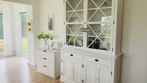A room with a white cabinet with glass doors, a white dresser, and a vase with flowers. - Diese Ferienwohnung Liegt im Erdgeschoss Eines Wunderschön Gelegenen Hauses mit Riesigem Grundstück in Nebel (Nebel)