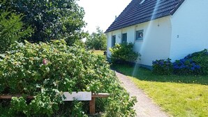 A white house with a number '5' on the side, surrounded by lush greenery and a gravel path leading to the entrance. - Diese Ferienwohnung Liegt im Erdgeschoss Eines Wunderschön Gelegenen Hauses mit Riesigem Grundstück in Nebel (Nebel)