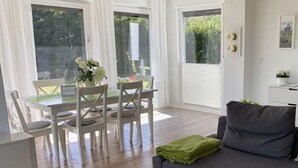 A modern living room with a grey sofa, a dining table with chairs, and a small kitchenette. - Diese Ferienwohnung Liegt im Erdgeschoss Eines Wunderschön Gelegenen Hauses mit Riesigem Grundstück in Nebel (Nebel)