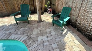 A patio area with two green Adirondack chairs, a wooden fence, and a brick pathway.