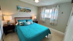 A bedroom with a bed, two bedside tables, a nightstand, a window with curtains, and a wall-mounted painting.
