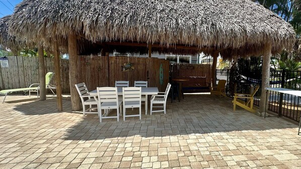 An outdoor seating area with a thatched roof, a pool, and a wooden fence.