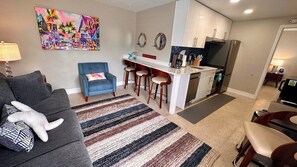 A compact living space with a sofa, a blue chair, a kitchen area with a refrigerator, and a colorful painting on the wall. - Turtle Nest 6 - Quick Walk to Beach (Fort Myers Beach)