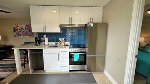A compact kitchen with white cabinets, a stainless steel refrigerator, a built-in oven, and a coffee maker.