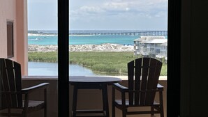 En balkon med to træstole og et bord, der giver udsigt over en strand med en færge i det fjerne.