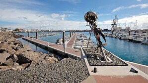 Ein Yachthafen mit vertäuten Booten, einer felsigen Küstenlinie und einer Skulptur.