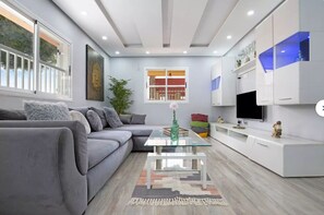 Un soggiorno moderno con un divano grigio, un tavolino da caffè in vetro e una TV su un mobile bianco.