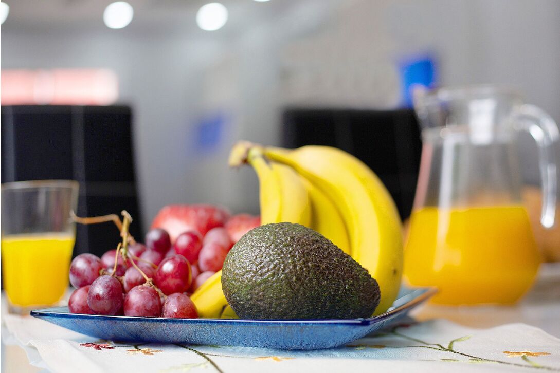 Een schaal met druiven, bananen en een avocado op een tafel.