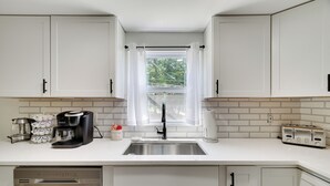Eine moderne Küche mit weißen Schränken, einer Edelstahl-Spüle, einer Kaffeemaschine und einem Toaster.