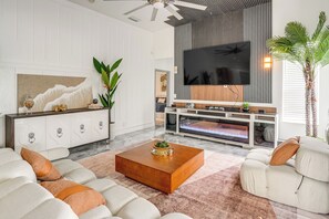 A modern living room with a flat-screen TV, a fireplace, a large plant, and a sofa set.