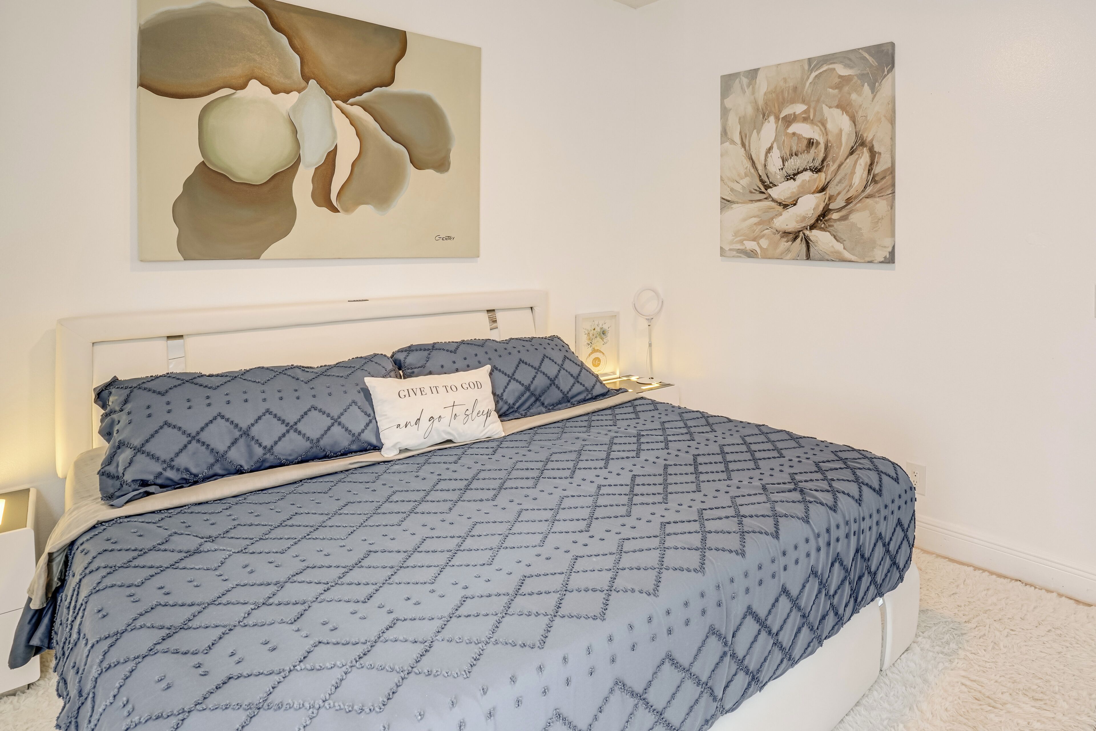 A bedroom with a bed, pillows, a nightstand, and wall art.