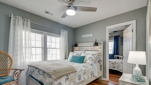 A bedroom with a bed, a chair, a nightstand, a ceiling fan, and a sign that reads "BEACH HOUSE". - Walk to Water: Coastal-Chic Home Near Myrtle Beach (Atlantic Beach)