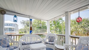 A covered outdoor seating area with wicker furniture and patterned cushions, overlooking a residential area with trees and a house. - Walk to Water: Coastal-Chic Home Near Myrtle Beach (Atlantic Beach)