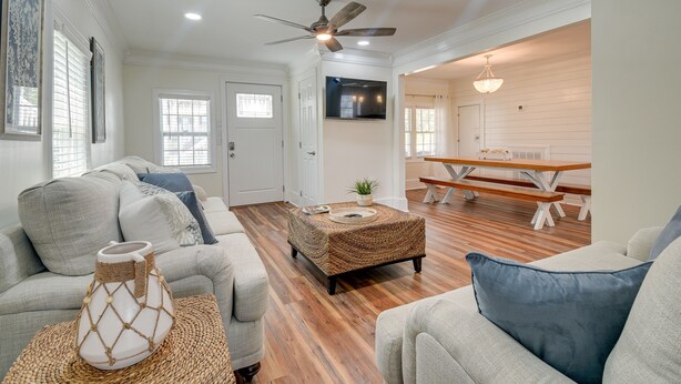 A spacious living room with a wooden floor, a ceiling fan, and a dining area with a bench and table. - Walk to Water: Coastal-Chic Home Near Myrtle Beach (Atlantic Beach)