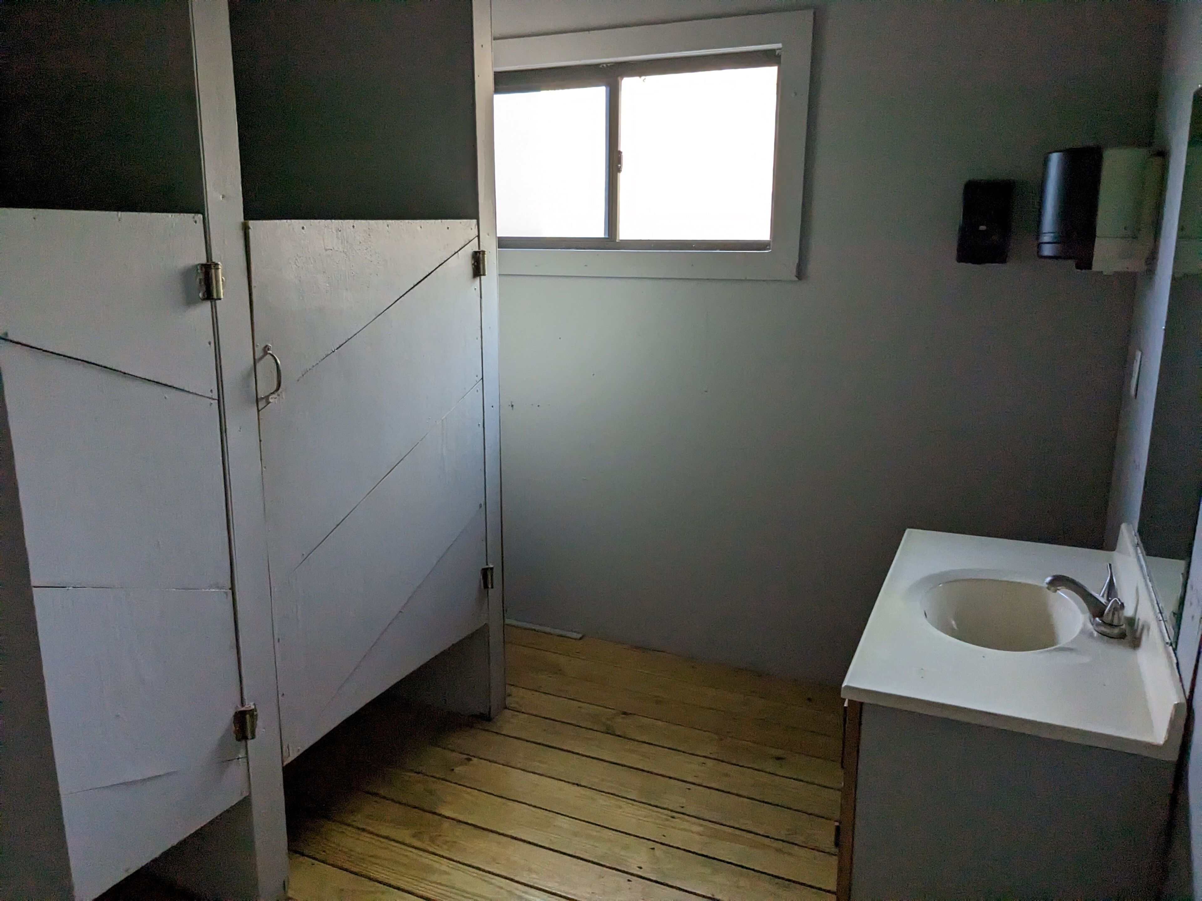 Un baño pequeño con piso de madera, un lavamanos blanco y una ventana.