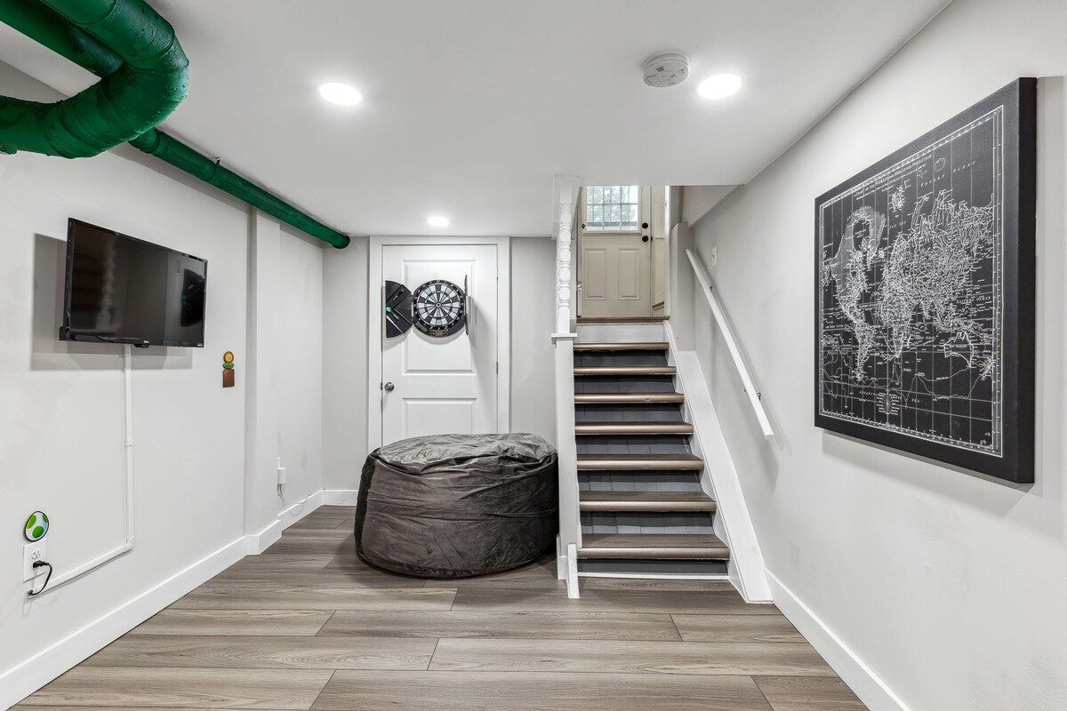 A hallway with a staircase, a television mounted on the wall, a dartboard, and a map.