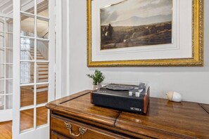 Una habitación con un escritorio de madera, un cuadro de un paisaje enmarco y un tocadiscos de vinilo.