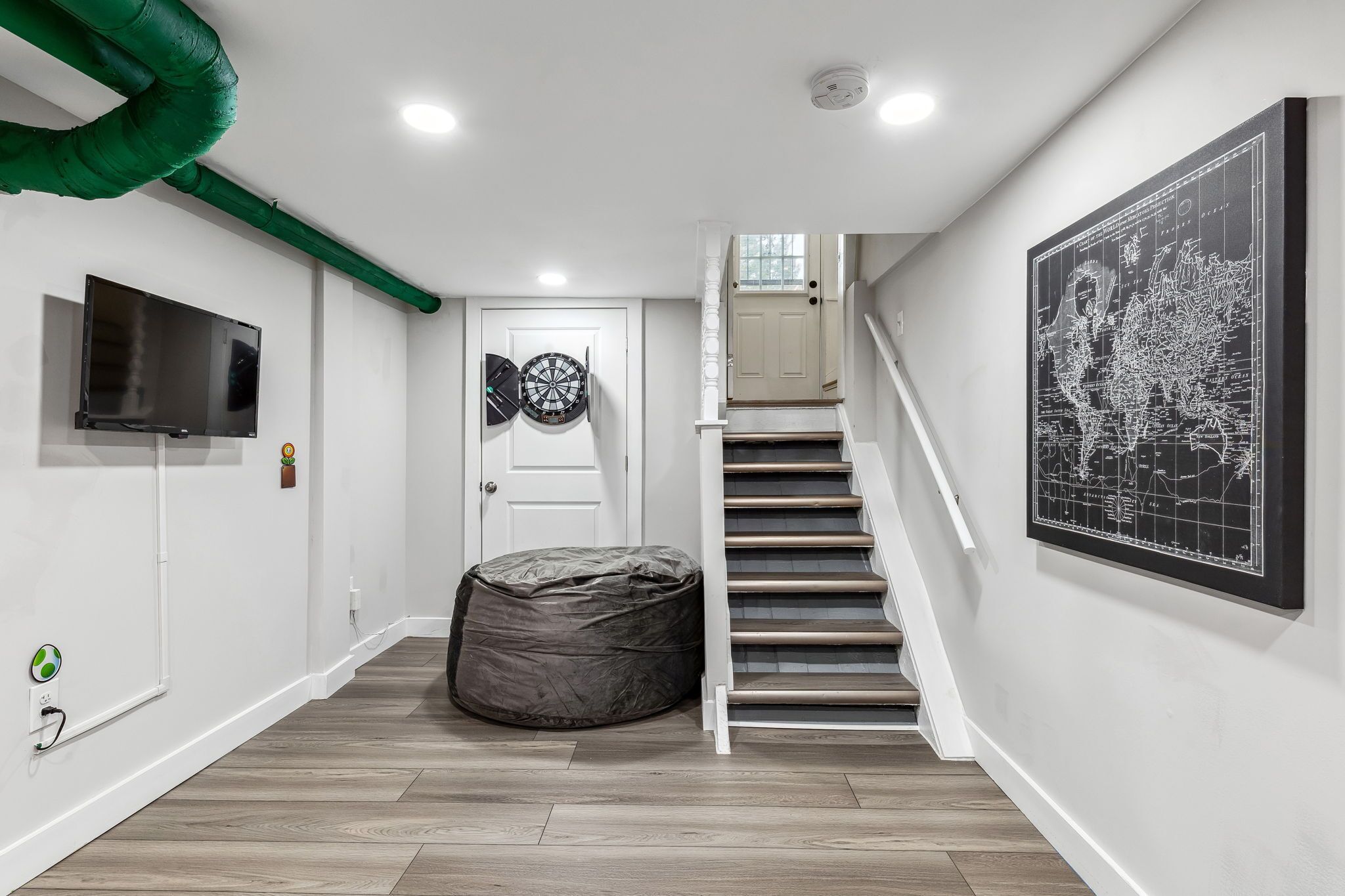 A hallway with a staircase, a television, a dartboard, and a map on the wall.