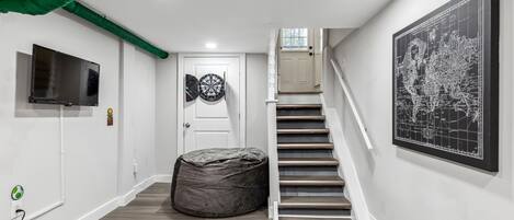 A hallway with a staircase, a television, a dartboard, and a map on the wall.