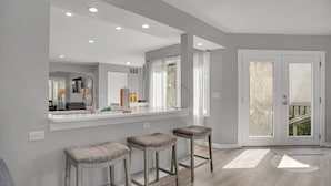 A modern kitchen with a white countertop, three bar stools, and a large mirror.