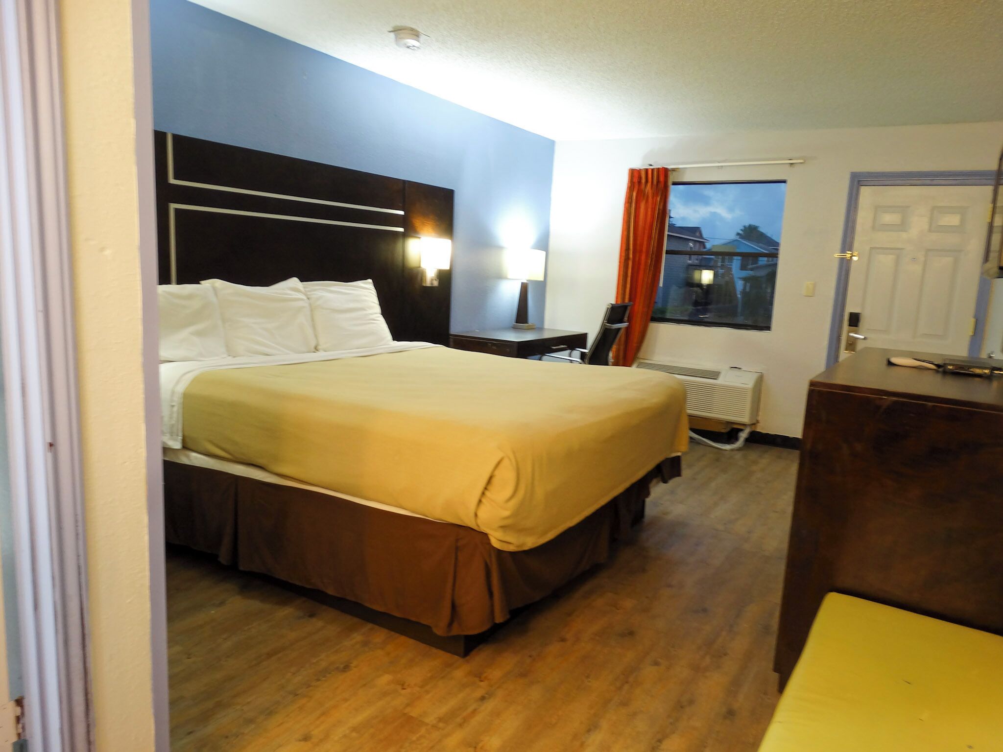 Habitación de hotel con cama, escritorio, silla, radiador y ventana con cortinas.