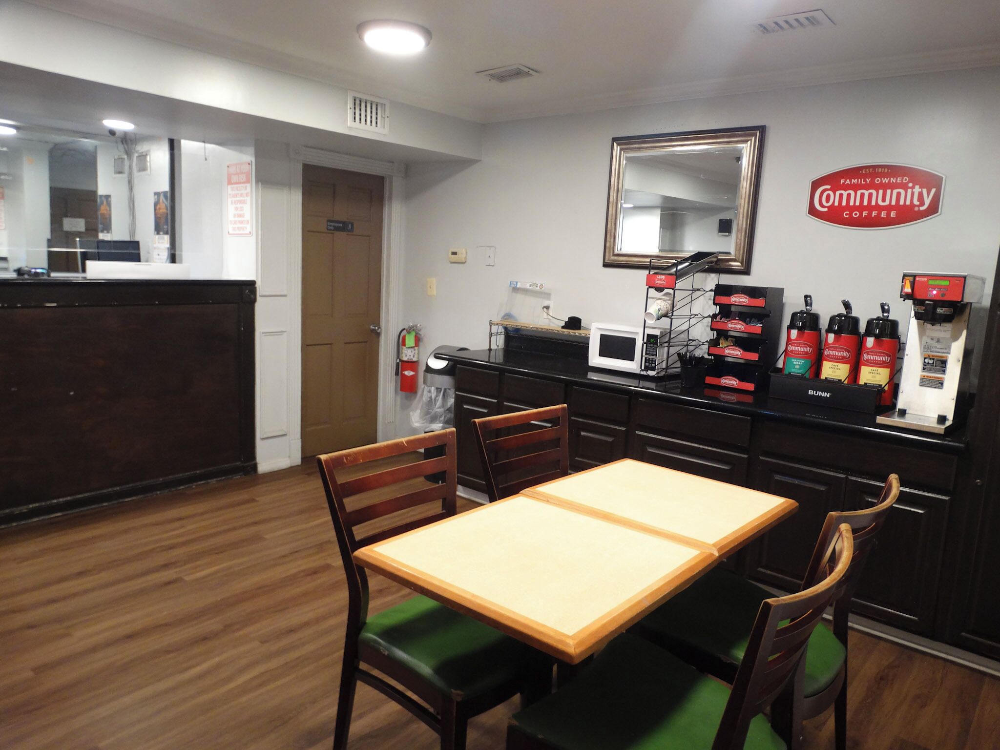 A small, clean room with a wooden table and chairs, a microwave, a coffee machine, and a mirror on the wall.