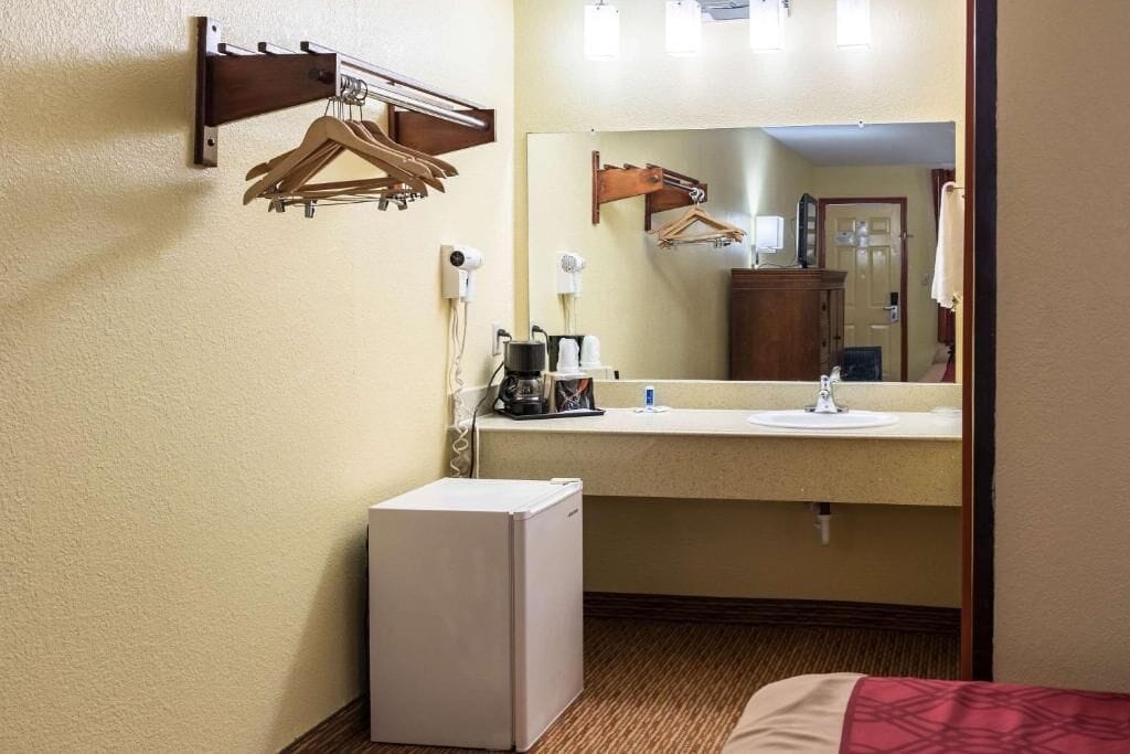 A hotel bathroom with a sink, mirror, and a small refrigerator.