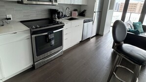 A modern kitchen with white cabinets, stainless steel appliances, and a bar stool.