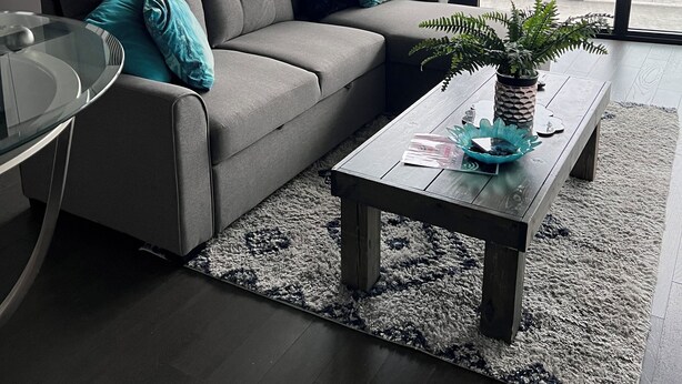 A modern living room with a grey sofa, a glass coffee table, and a view of the city through large windows.