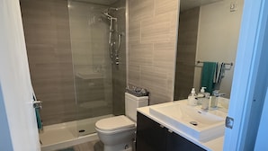 A modern bathroom with a glass-enclosed shower, a toilet, a sink, and a mirror.