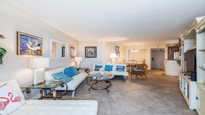 A spacious living room with a sofa, coffee table, and dining area. There are framed artworks on the walls and a large mirror. - Views of Tigertail Beach and sunsets (Marco Island)
