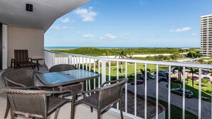A balcony with wicker furniture, a glass table, and a view of a beach and ocean. - Views of Tigertail Beach and sunsets (Marco Island)