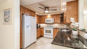 A kitchen with wooden cabinets, a refrigerator, a microwave, an oven, and a granite countertop. - Views of Tigertail Beach and sunsets (Marco Island)
