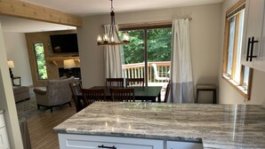 A modern kitchen with a marble countertop, white cabinetry, and a dining area with a table and chairs. - Updated Phase 2 Hideaway Valley Condo Nestled in the Woods (Harbor Springs)