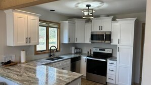 A modern kitchen with white cabinets, a granite countertop, a built-in microwave, and a stainless steel oven. - Updated Phase 2 Hideaway Valley Condo Nestled in the Woods (Harbor Springs)