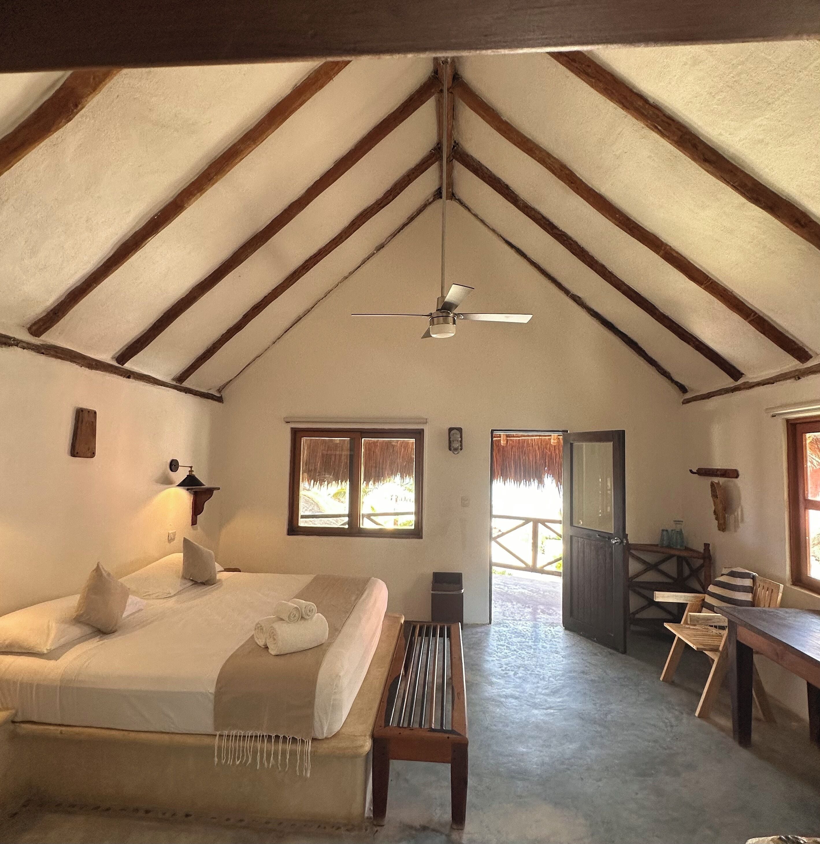 A cozy room with a bed, a bench, a desk, and a ceiling fan.