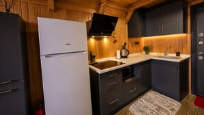 Una cocina compacta con paredes de madera, un refrigerador blanco, armarios oscuros y una estufa integrada.