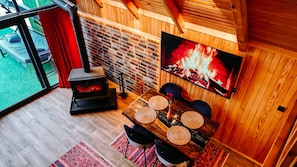 Une pièce chaleureuse avec une cheminée, une table à manger agrémentée de sets de table en fibres tressées et un téléviseur diffusant une image de feu de cheminée.