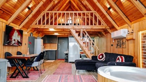 A cozy cabin interior with a dining area, kitchen, living room, and a staircase leading to an upper level.