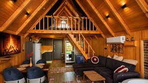 Un loft espacioso con techo alto, vigas de madera, una chimenea acogedora, un comedor, una sala de estar con sofá y un jacuzzi.