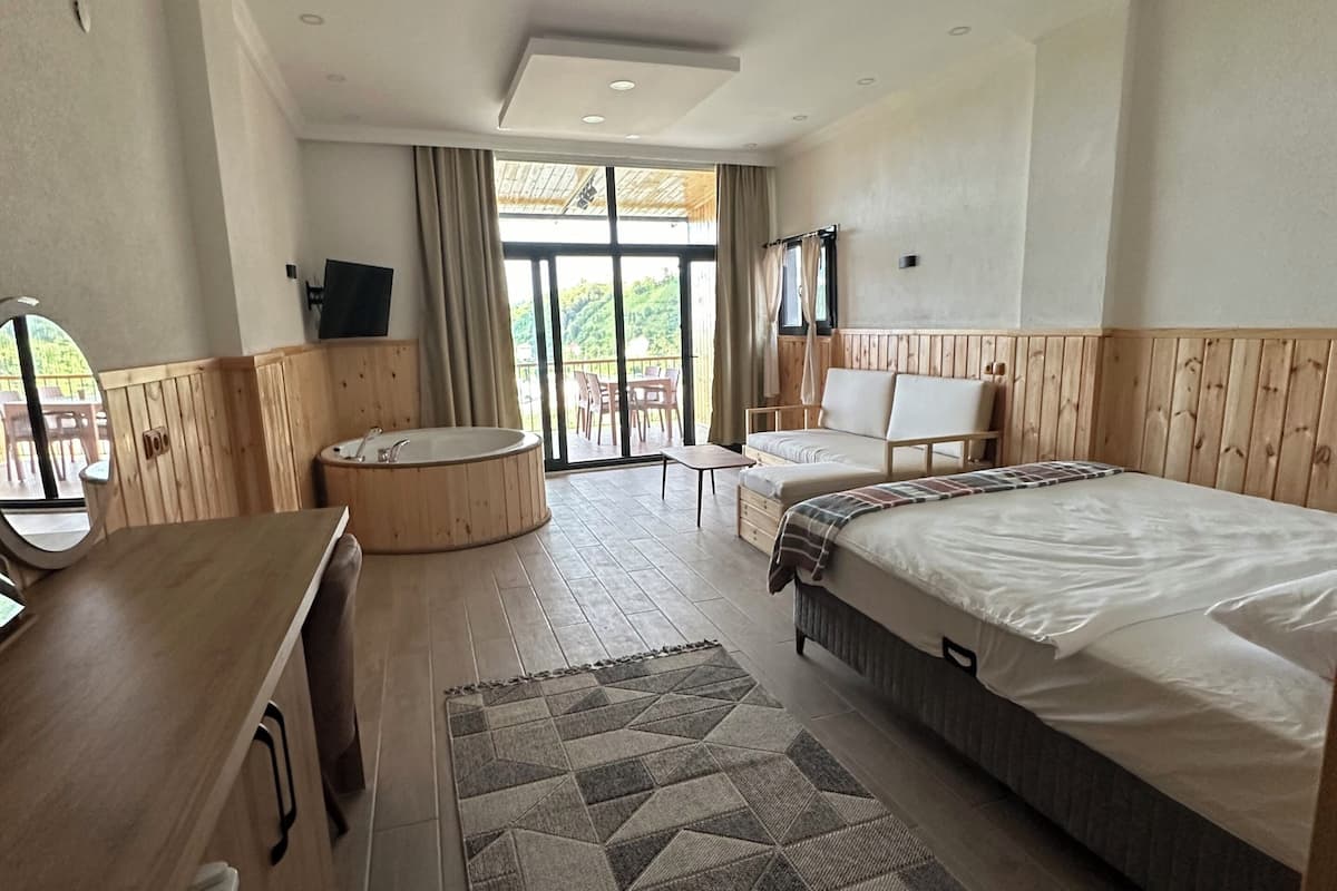 A hotel room with a bed, a desk, a TV, a balcony with a table and chairs, and a large window.