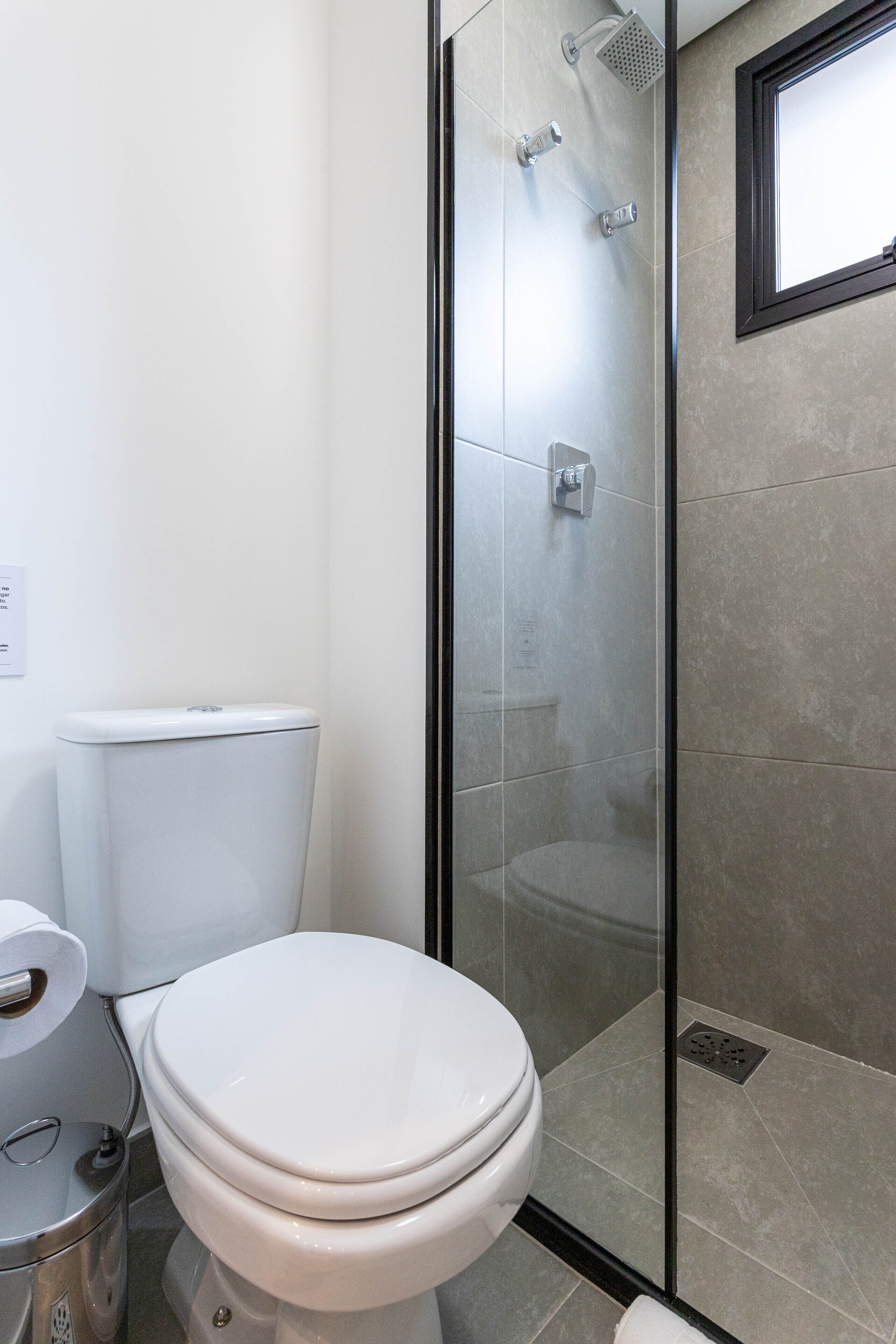 A modern bathroom with a toilet, a glass-enclosed shower, and a wall-mounted toilet paper holder.