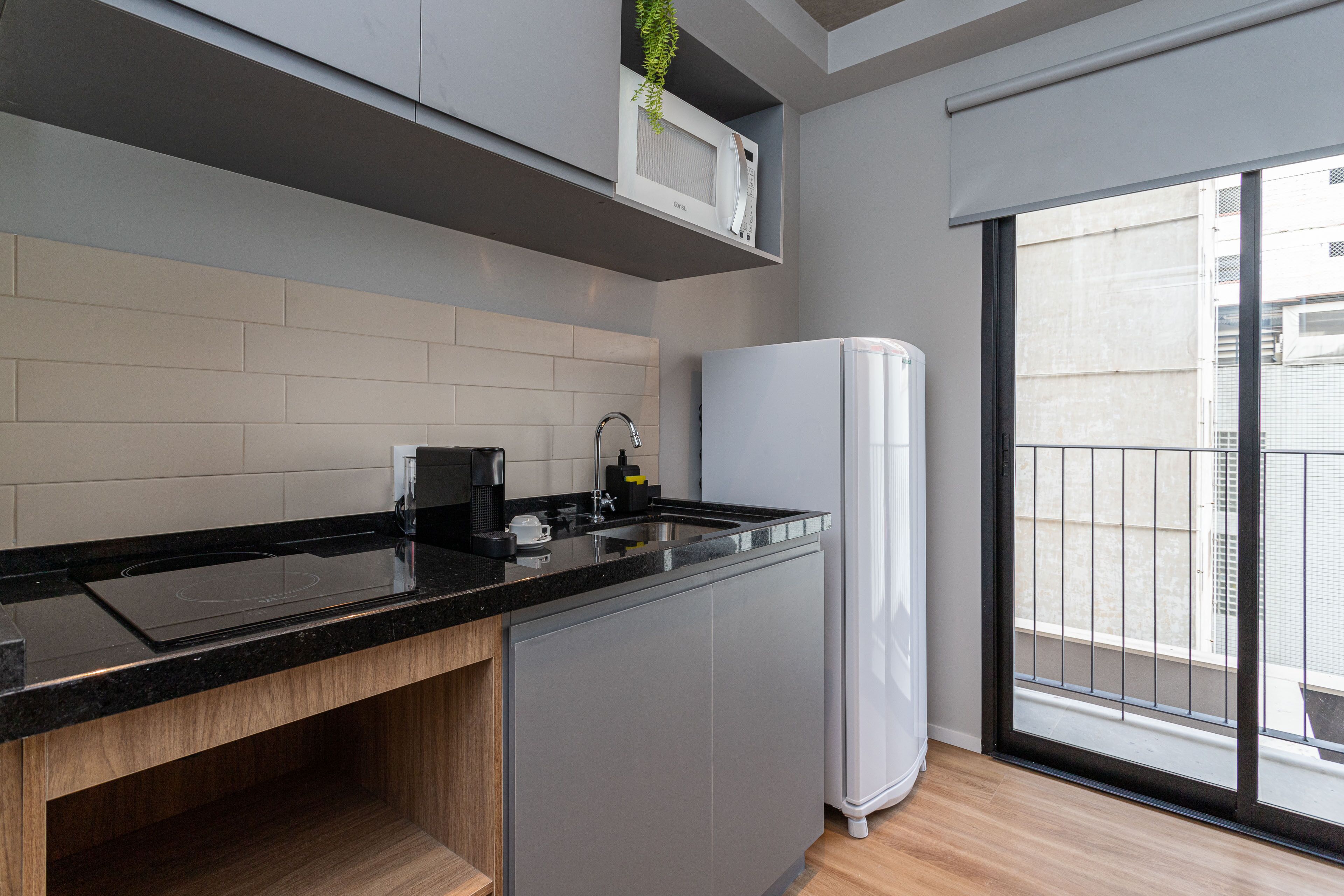A modern kitchen with a black countertop, grey cabinets, a white refrigerator, and a window with a view of buildings.