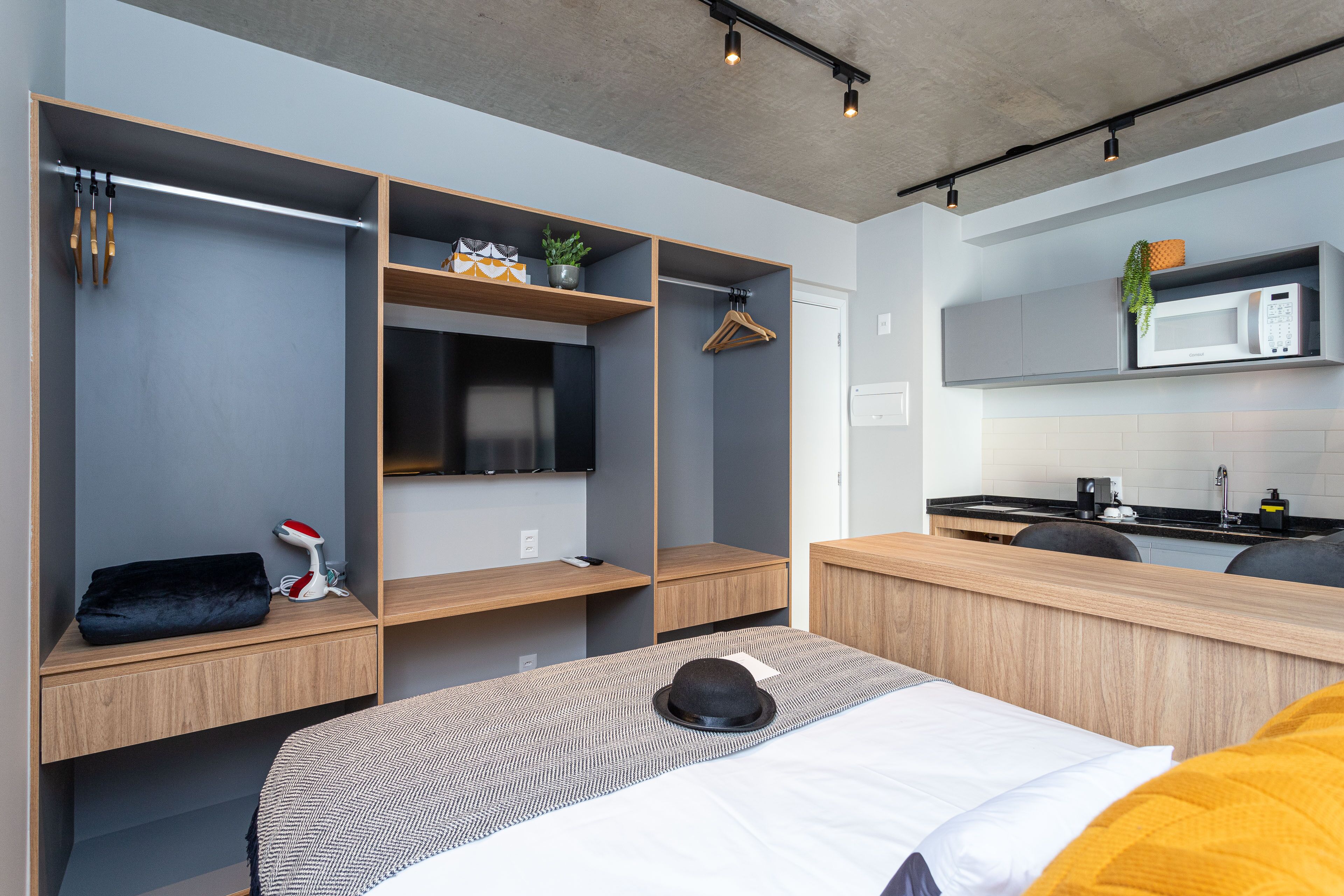 Habitación de hotel compacta con cama, escritorio, kitchenette y estanterías empotradas.