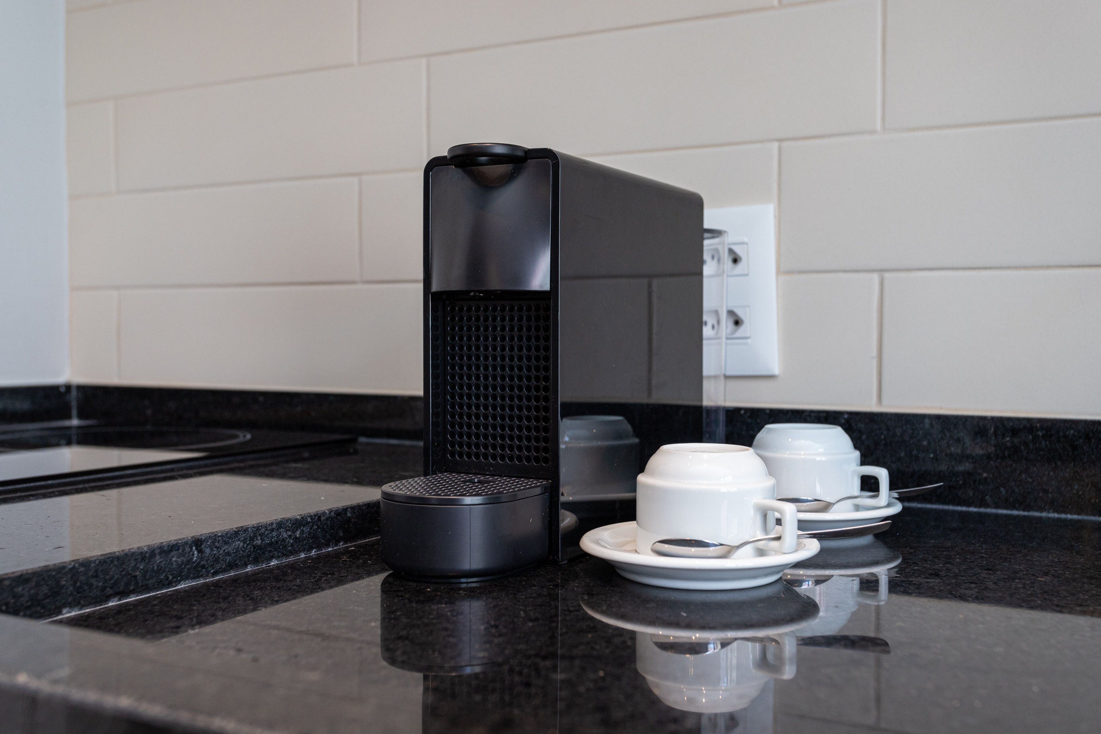 A coffee maker and two white cups on a black countertop.