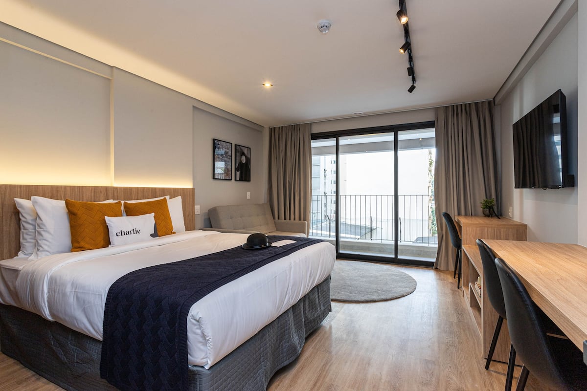 Ein modernes Hotelzimmer mit einem großen Bett, einem Schreibtisch und Blick auf die Stadt vom Balkon aus.