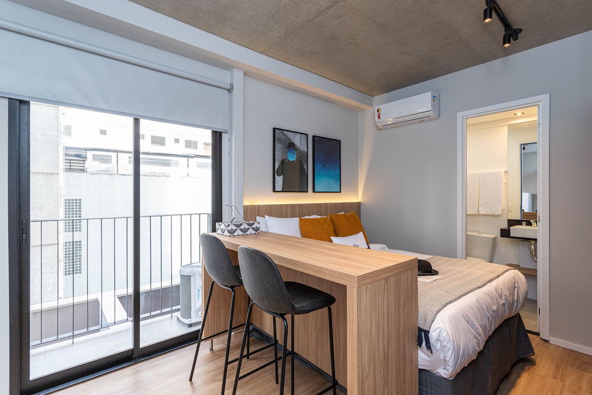 Ein modernes Schlafzimmer mit großem Fenster, einer kleinen Bar und einem Bett mit Kopfteil.