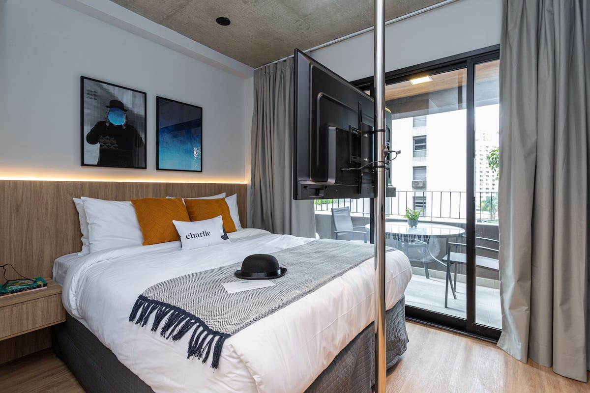 Ein modernes Hotelzimmer mit einem großen Bett, einem an der Wand montierten Fernseher und einem Balkon mit Sitzgelegenheit.