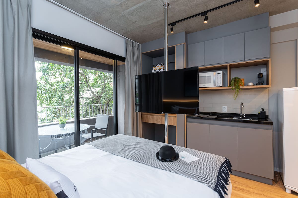 Ein modernes Hotelzimmer mit einem großen Bett, einem Flachbildfernseher, einer kleinen Küchenzeile und einem Balkon mit Tisch und Stühlen.