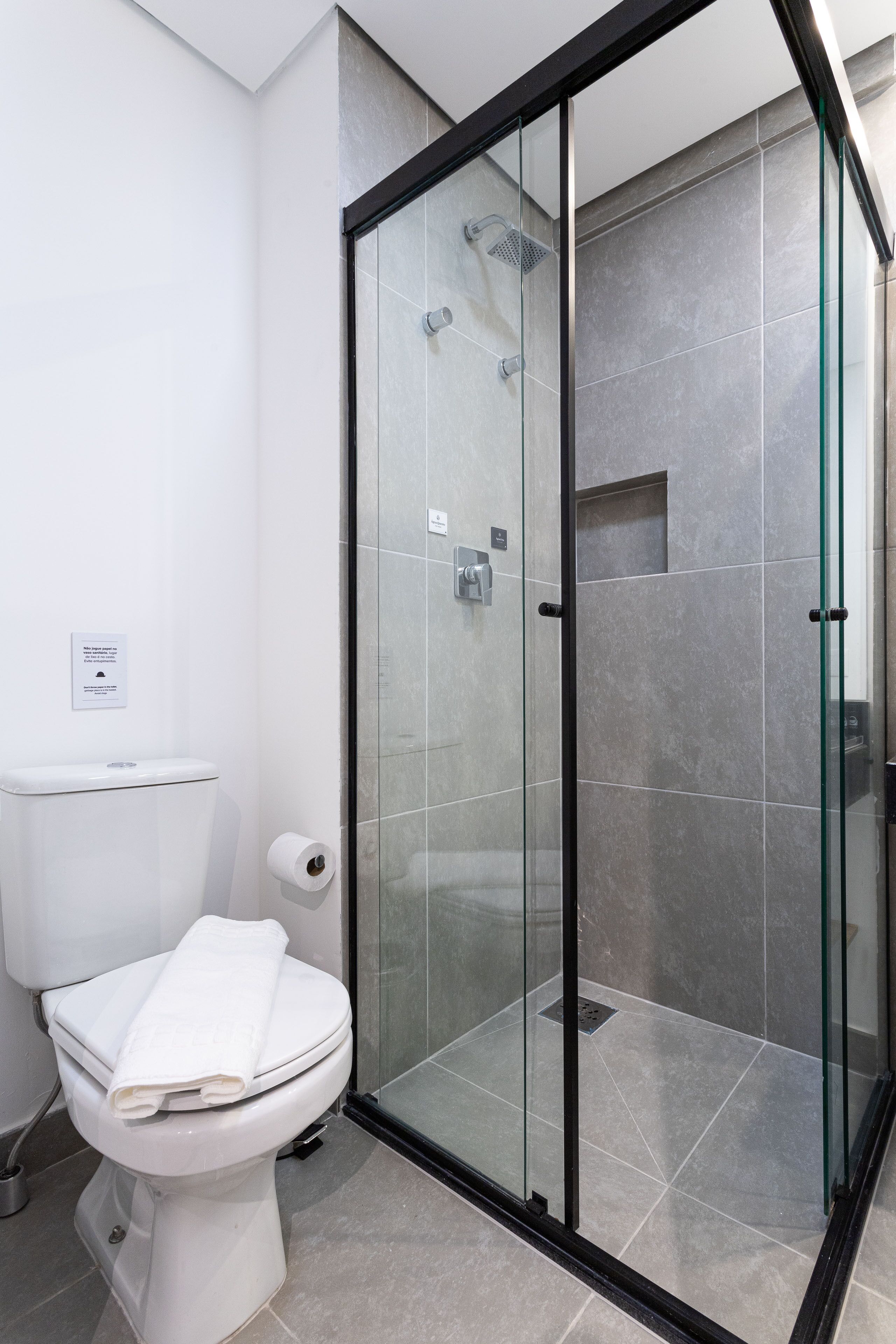A modern bathroom with a glass-enclosed shower, a toilet, and a roll of toilet paper.